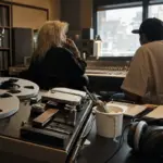 Registratore a bobine in studio con gelato che cola e mini Statua della Libertà, due musicisti sfocati al mixer