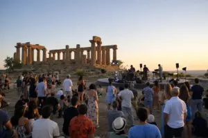 Pubblico a un concerto al tramonto davanti a un tempio antico, con palco circolare e luci sul sito archeologico