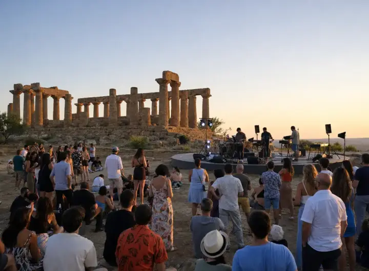 Pubblico a un concerto al tramonto davanti a un tempio antico, con palco circolare e luci sul sito archeologico